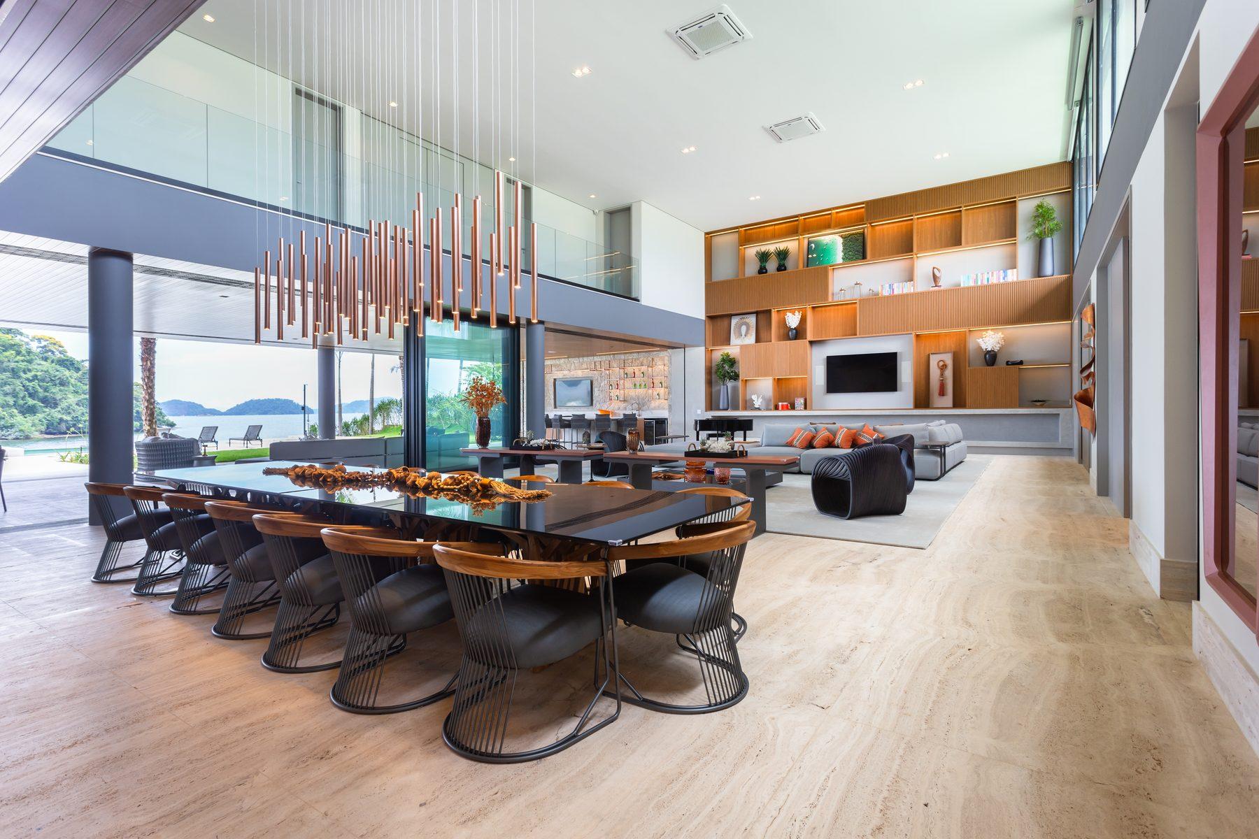 Salão de pé-direito duplo com mesa de jantar para doze, living integrado e vidro aberto para o mar e as ilhas de Angra