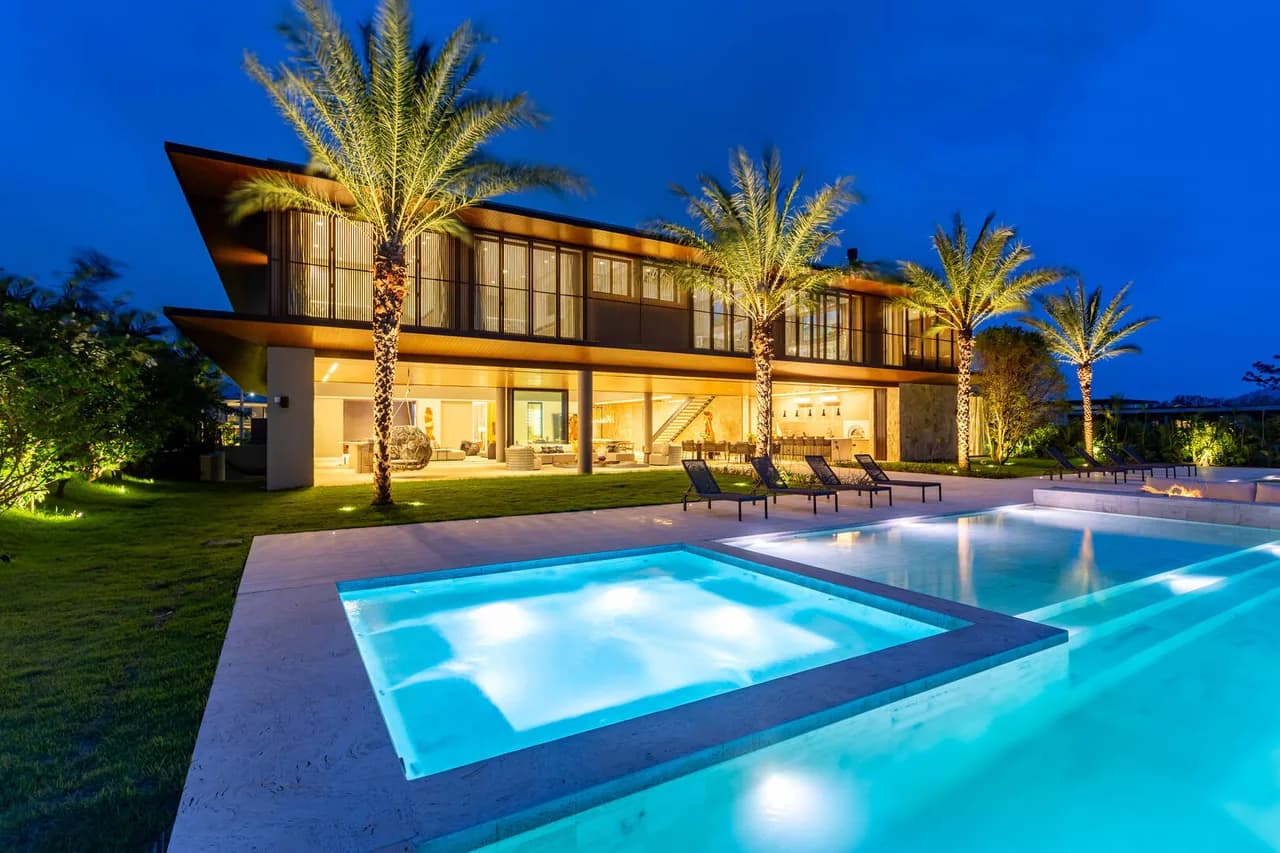 Residência moderna iluminada ao crepúsculo, com piscina e palmeiras