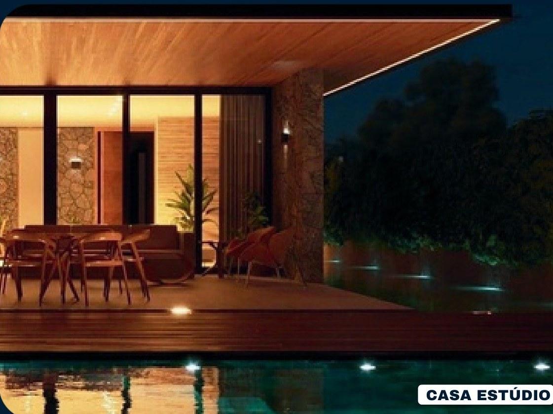 Casa Estúdio à noite, com deck de madeira, piscina iluminada e sala aberta para fora