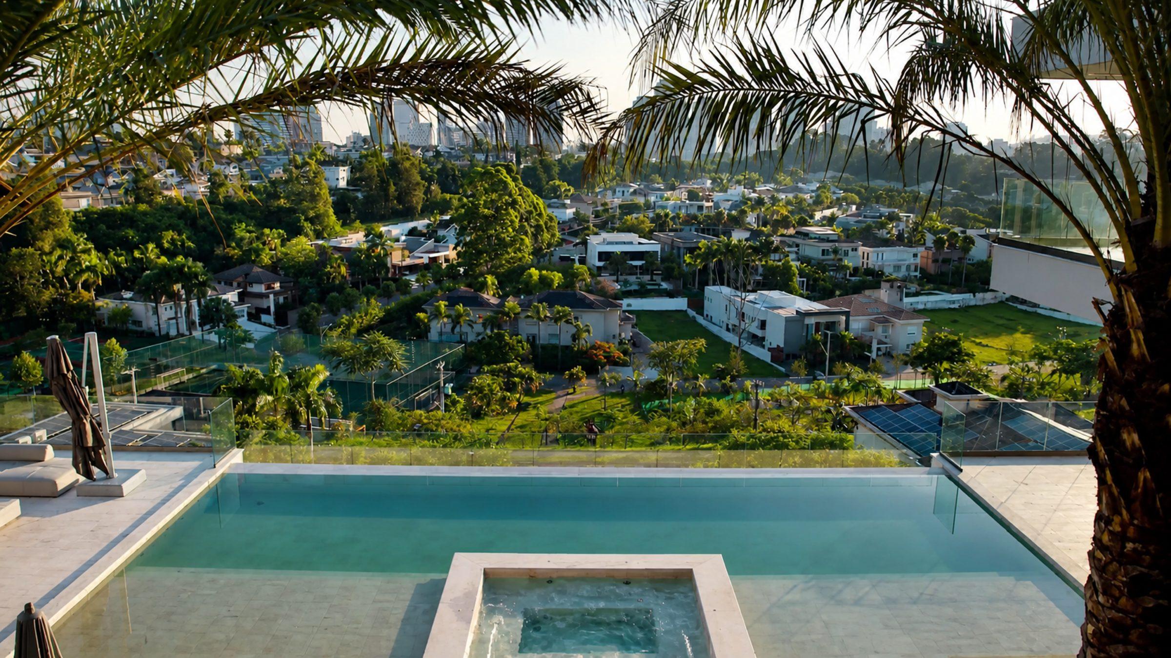 Piscina de borda infinita com vista para as casas e a mata do condomínio, ao entardecer